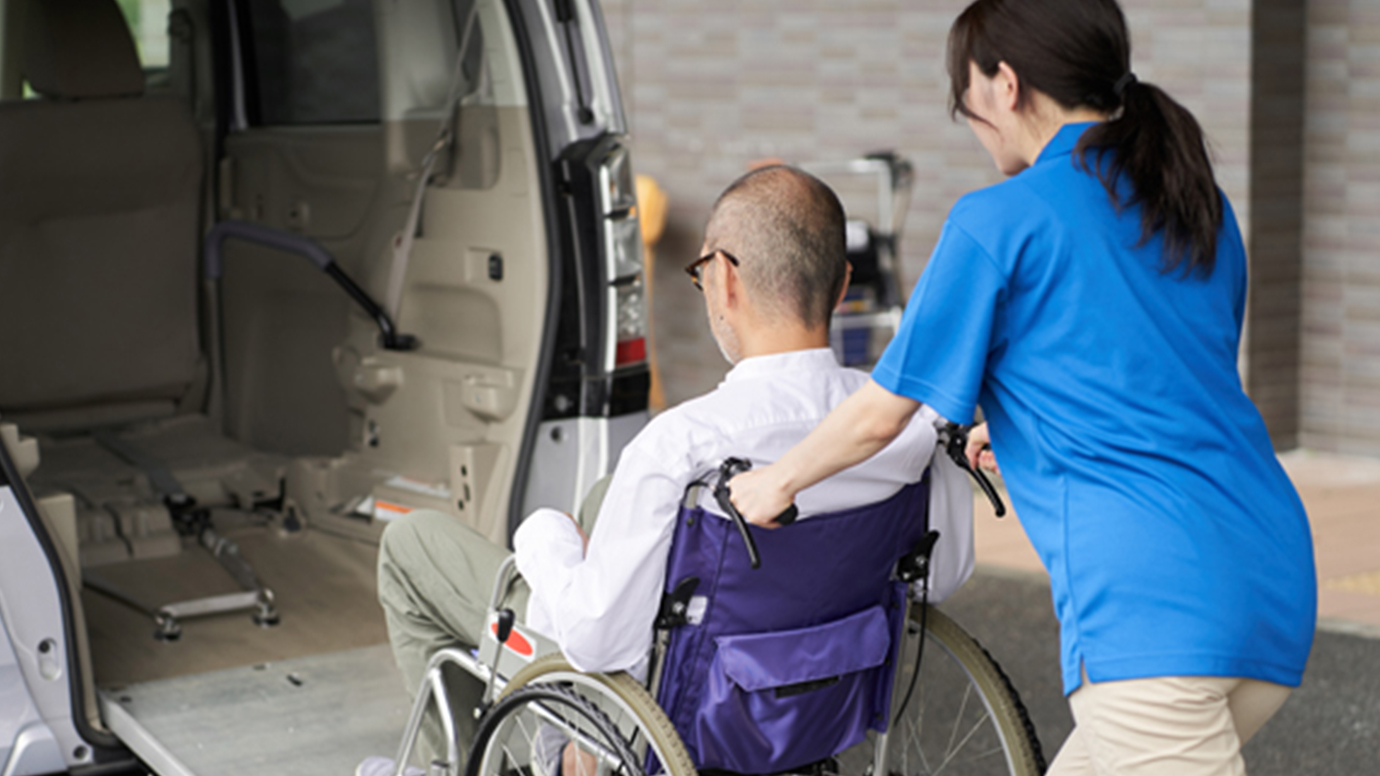 A young woman pushes a man in a wheel chair up a ramp into an accessible van.