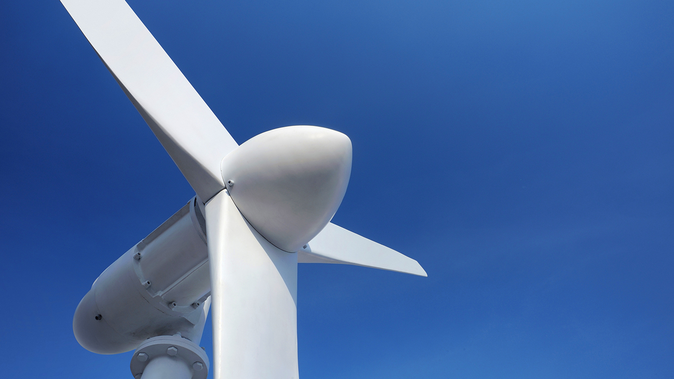 A white wind turbine against a clear blue sky.