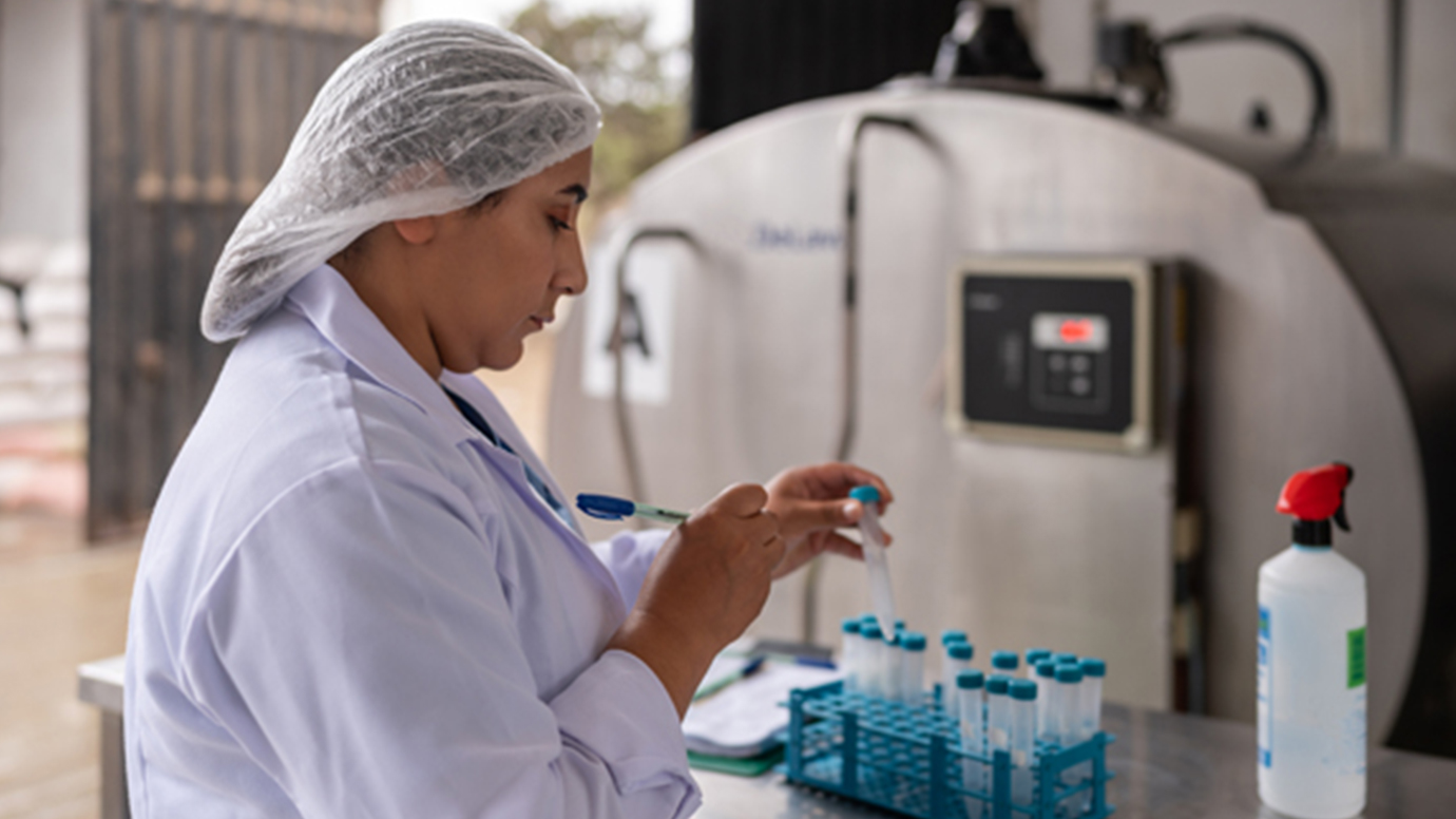 A BIPOC woman in a lab coat and hair net tests water samples in an industrial plant.