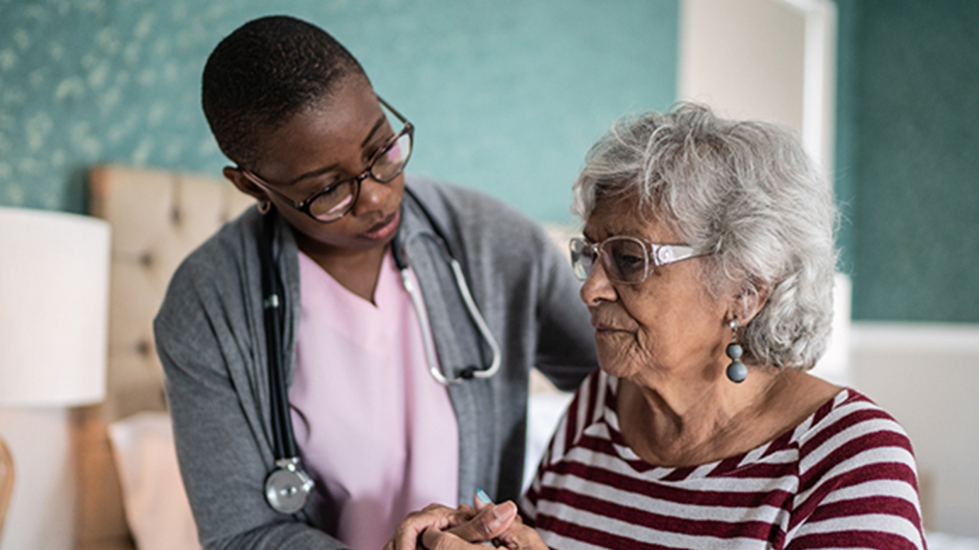 An African American health care worker holds the hand of an elderly Black woman.