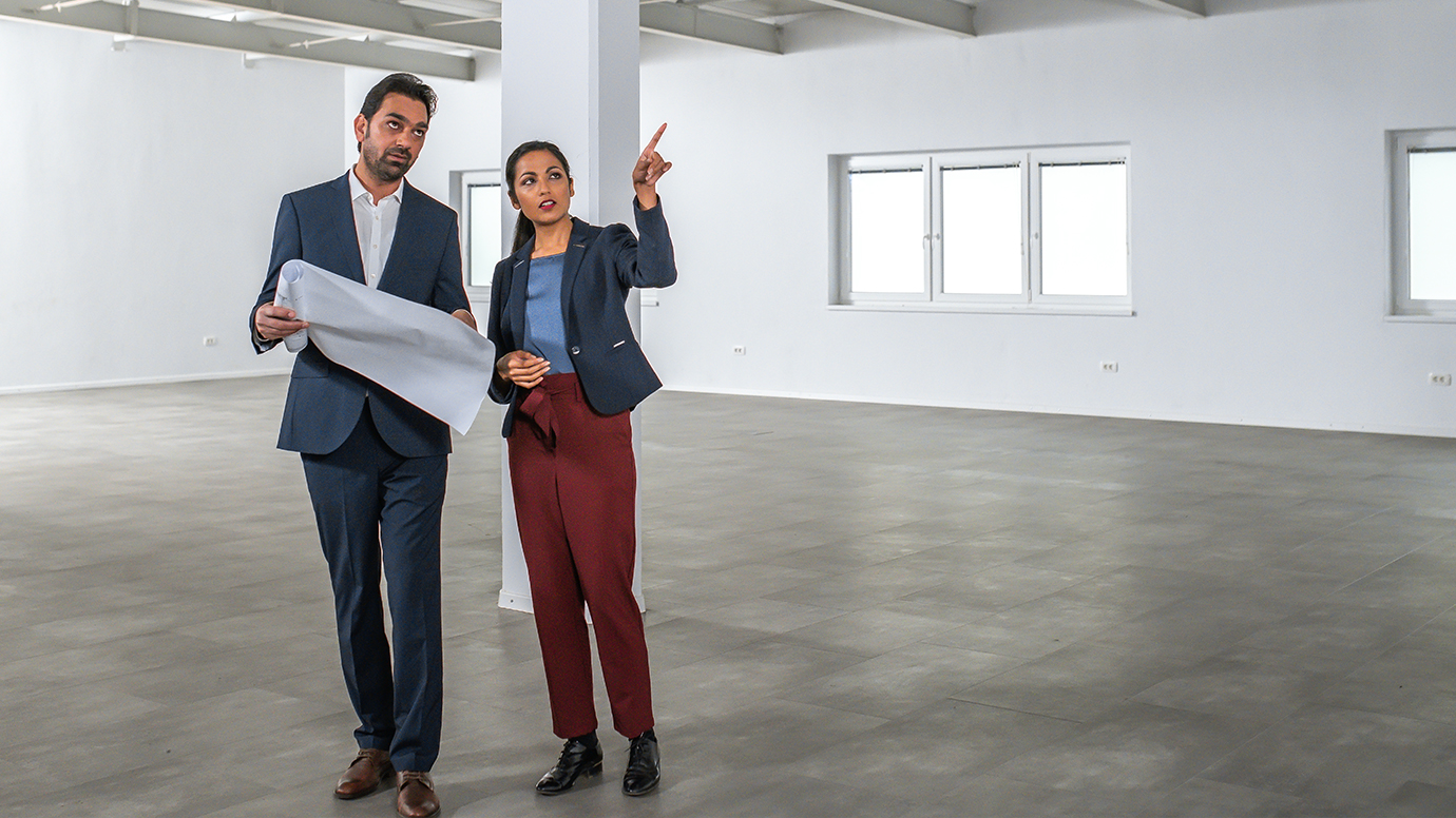 Two BIPOC business people discuss building plans while standing in a an empty chimerical space.