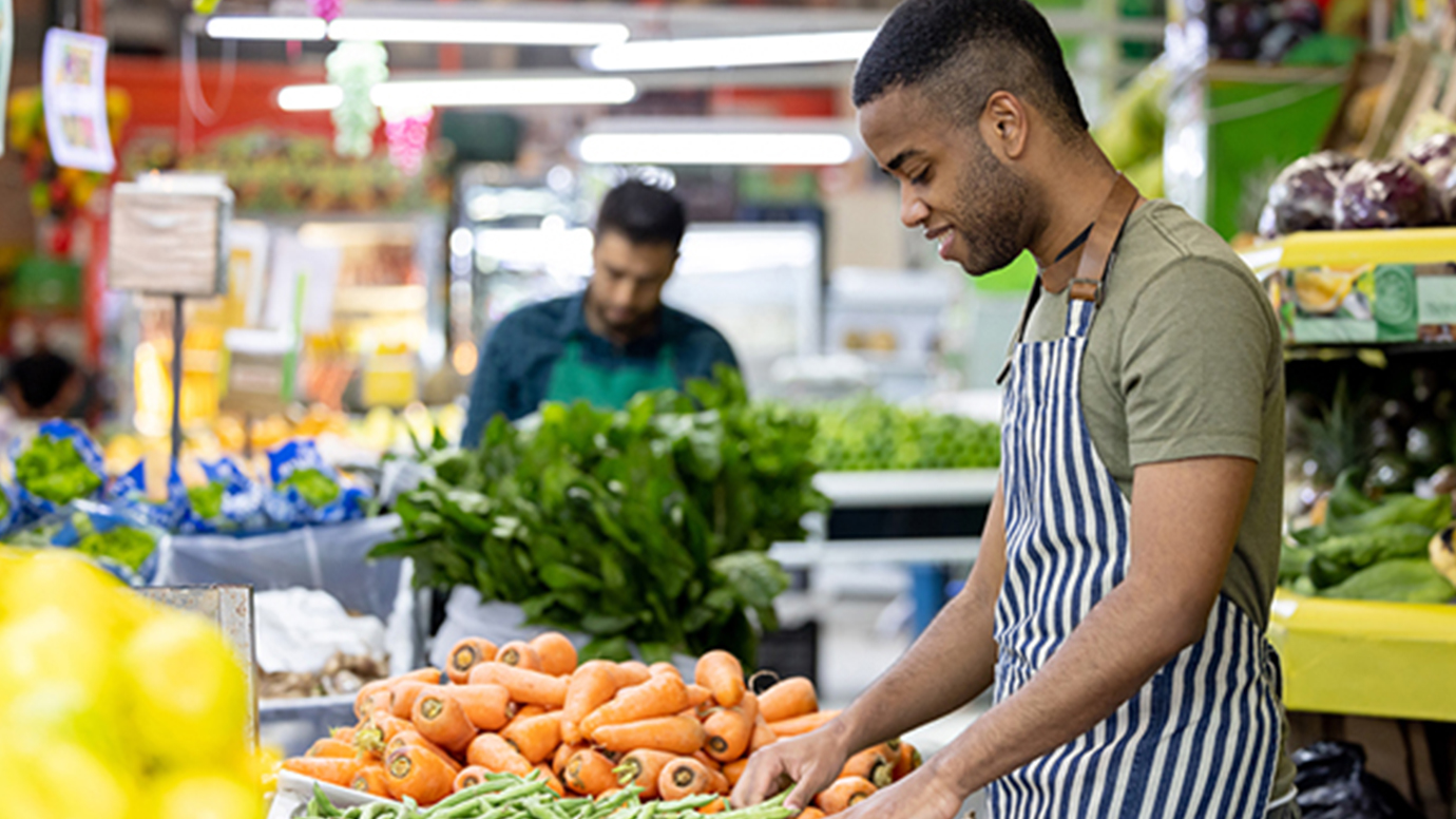 Two BIPOC men sort vegetables in the produce section of a grocery store.